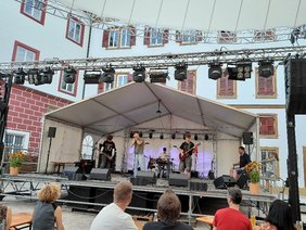4 Musiker auf Bühne, 2 Gitarristen, 1 Person am Keyboard und eine am Schlagzeug, bühne steht in einem Schlosshof