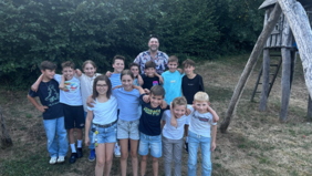 Kindergruppe mit Gitarrenlehrer Andi Zanker blicken lachend in die Kamera, stehen im Freien